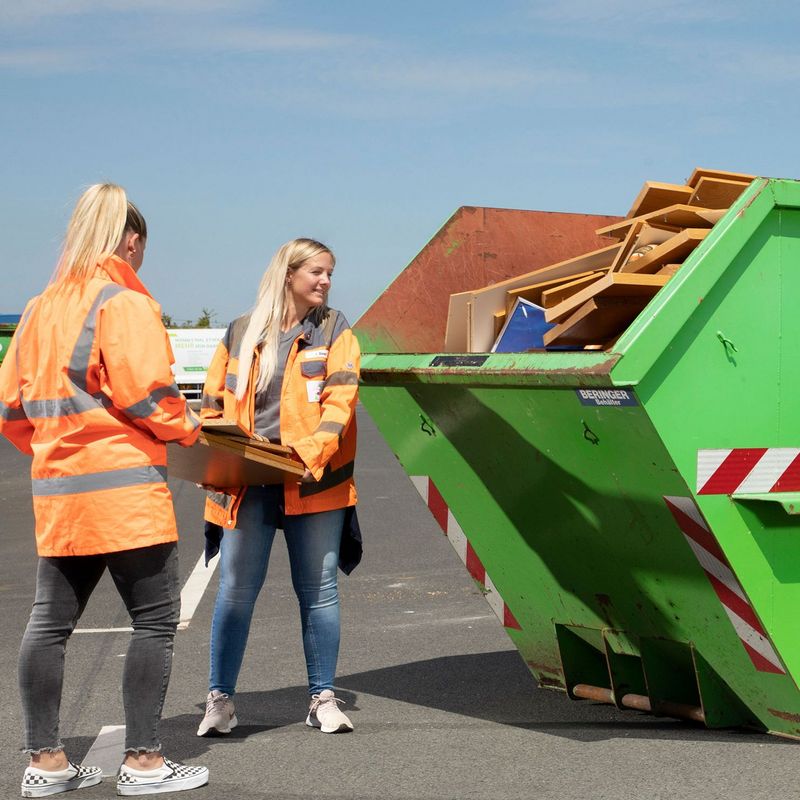 Zwei Mitarbeiterinnen werfen Möbel in Container